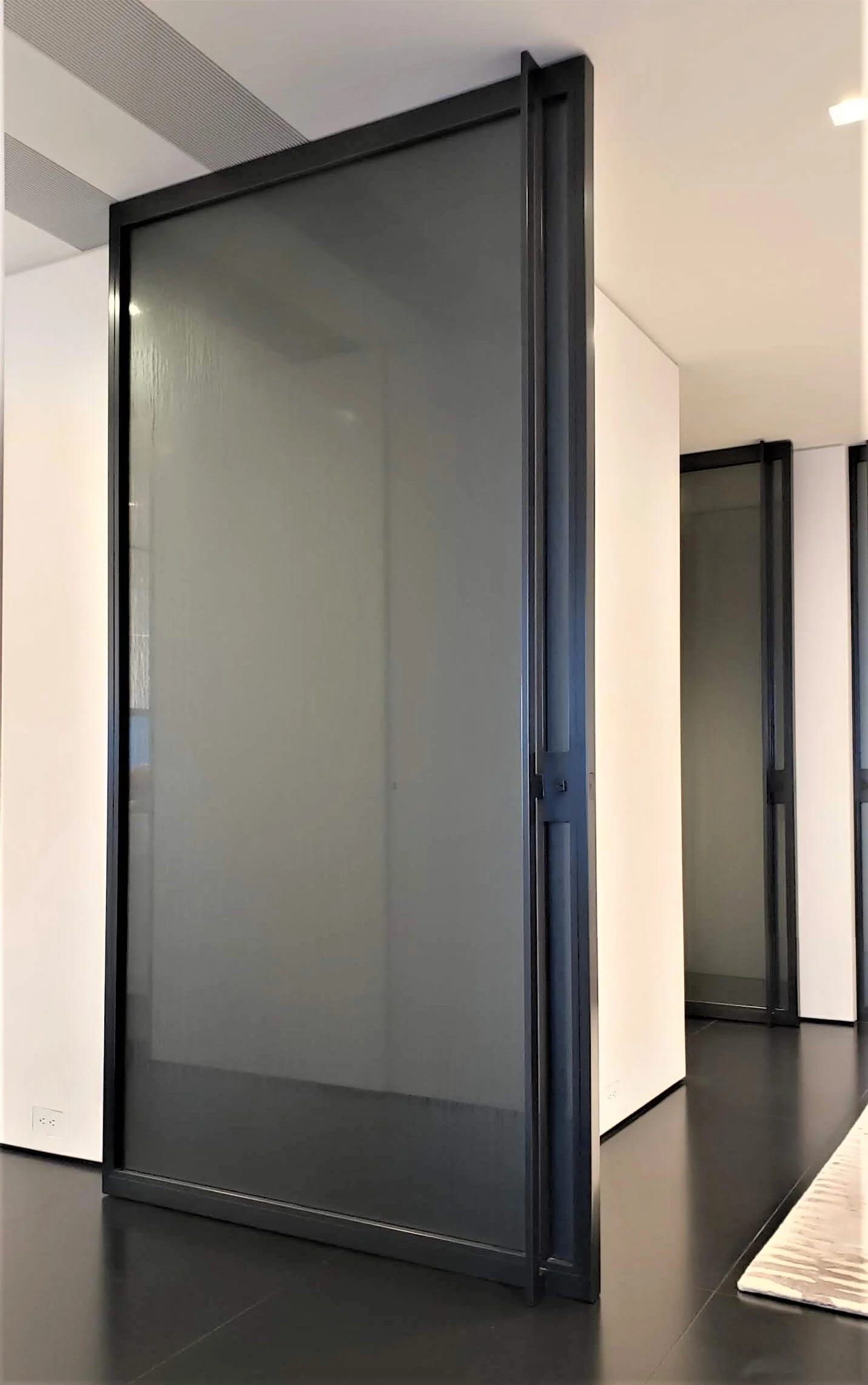 Blackened stainless steel pivot door with glass, standing open