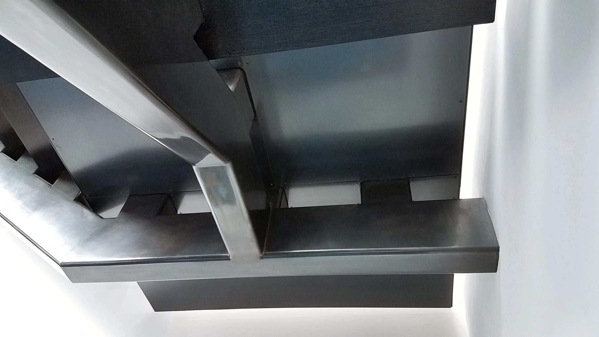 Blackened steel stair stringer carrying floating treads, seen from below