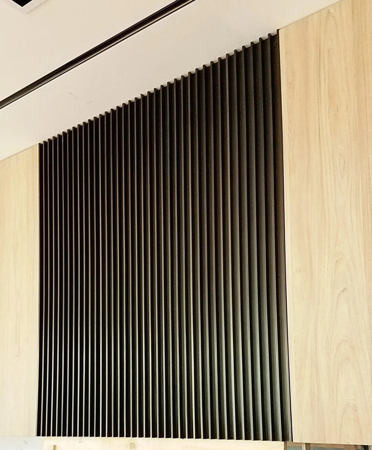 Screen of vertical blackened steel fins against a timber wall