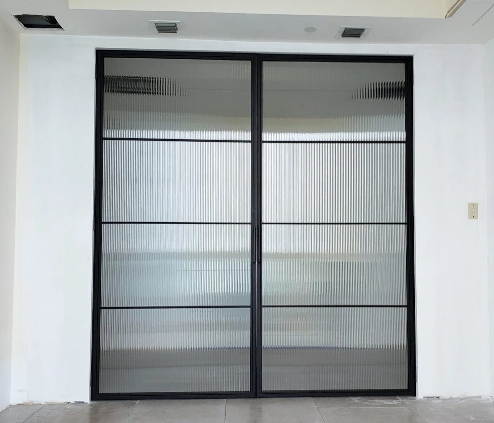 Pair of powder-coated steel doors with horizontal muntins and reeded glass