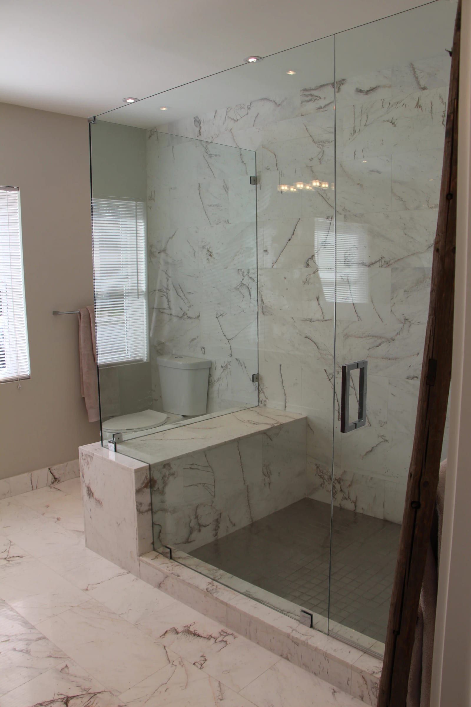 Frameless glass shower with marble walls and a bench